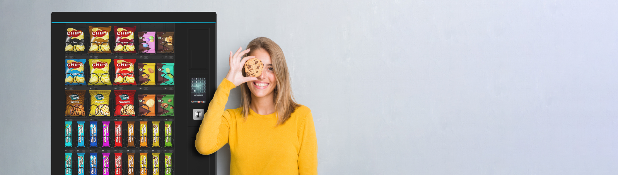 In front of a grey wall stands a Sielaff combi/spiral machine, next to it a woman holding a biscuit in front of her eye.